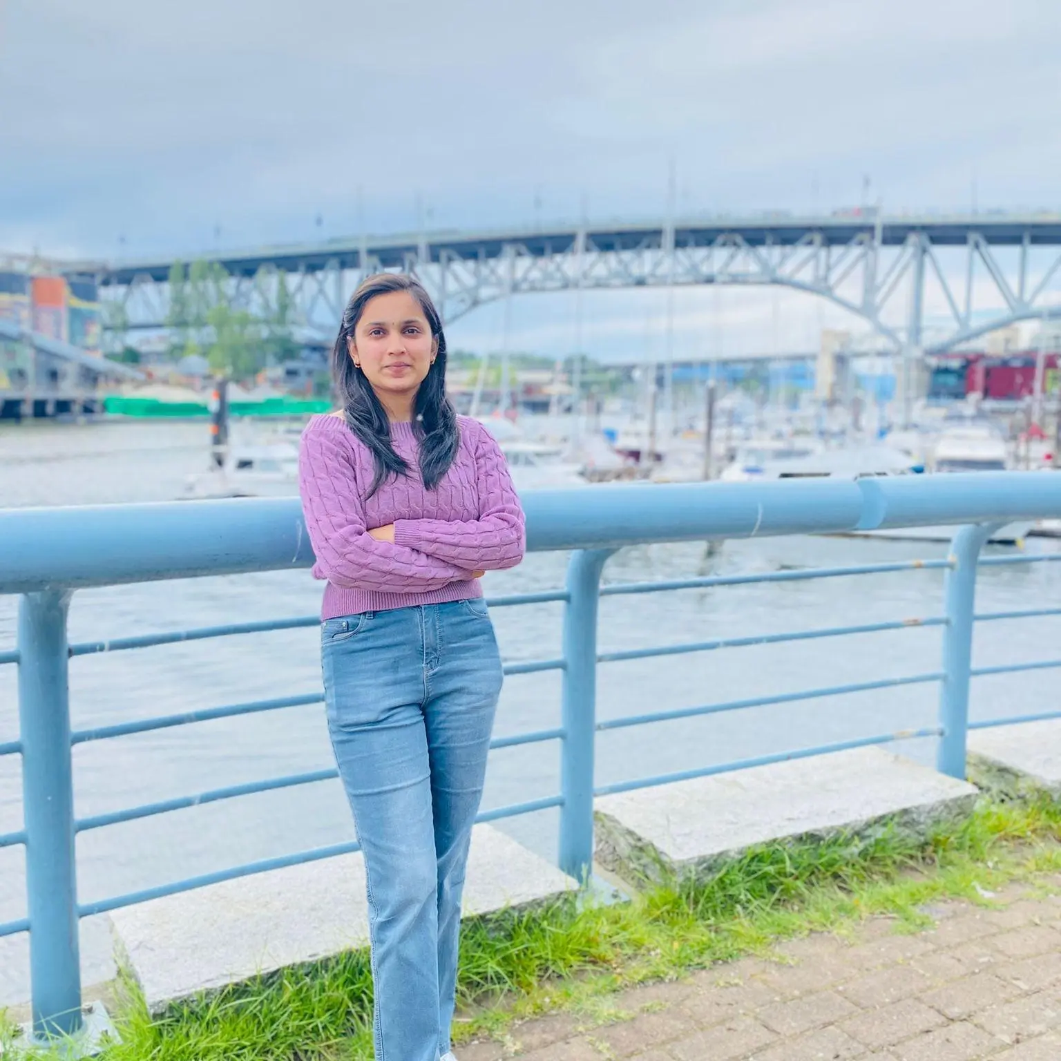 Home Prerna Bansal from Canada, standing by a waterfront in a purple sweater — Zelora Naturals™ customer testimonial.