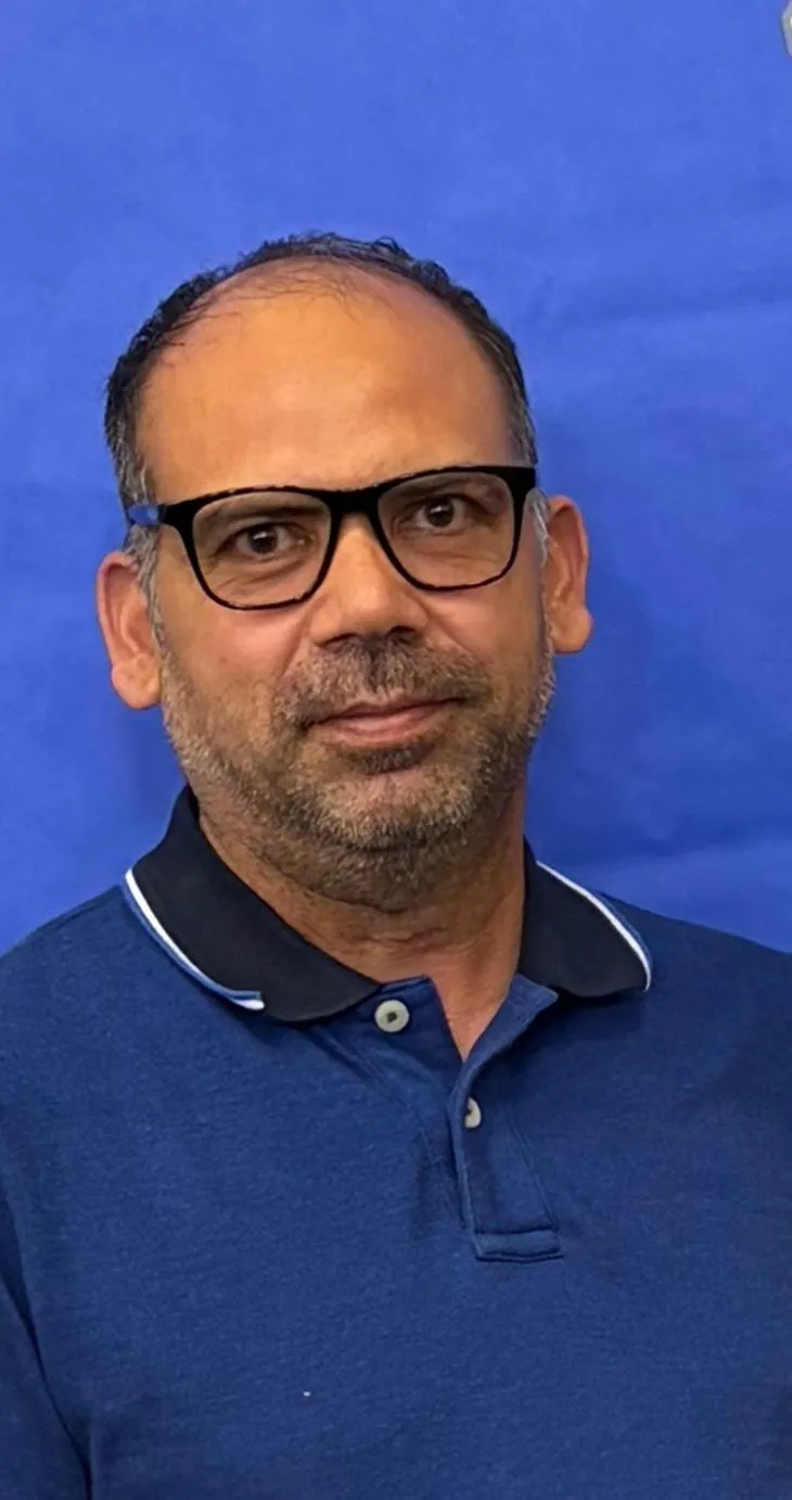 Home Portrait of Dharminder Singh Bedi from the USA, wearing glasses and a blue polo shirt.